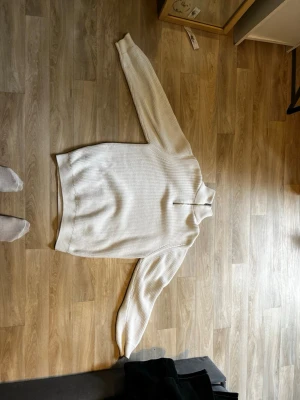 Vit stickad halvzip-tröja från Zara. Vi kan förhandla - Säljer en vit stickad tröja från Zara med halv dragkedja och hög krage. Tröjan har en ribbstickad struktur och långa ärmar, perfekt för lager-på-lager och chill stil.