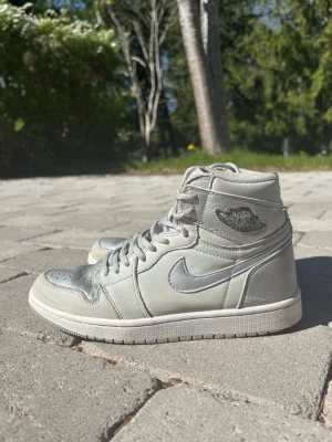 Nike Air Jordan 1 Retro High OG CO.JP "Tokyo" - Snygga Nike Air Jordan 1 High sneakers i en stilren grå och metalliskt silverfärgad design. Material: Läderöverlägg i metallic silver kombinerat med grå mocka.Detaljer: Klassisk Air Jordan Wings-logotyp på sidan och perforerad tåbox. 