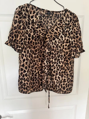 Leopardmönstrad blus från shein - Snygg leopardmönstrad blus från shein med volangkant längs knäppningen och korta ärmar. Blusen har en lös passform och är tillverkad i ett lätt, glansigt material som känns skönt mot huden. Perfekt för dig som gillar djurmönster och vill sticka ut. Använd 2 eller 3 gånger max