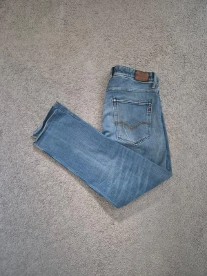 Replay - Säljer ett par klassiska ljusblå jeans från Levi's med raka ben och snygga detaljer på bakfickan. Jeansen har en brun patch vid linningen och är tillverkade i slitstark denim. Perfekta för en avslappnad och trendig look.