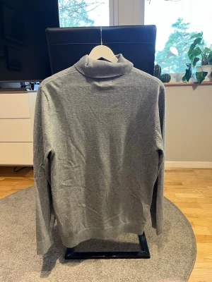 Grå polotröja i stickat material - En stilren grå stickad polotröja med lång ärm och klassisk passform. Tröjan har en mjuk och följsam känsla, perfekt för lager-på-lager. Enkel design utan synliga loggor eller mönster, vilket gör den lätt att matcha med olika outfits.