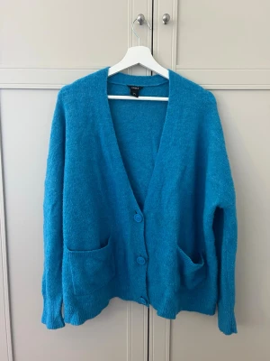 Blå oversized kofta med fickor - Mysig oversized blå stickad kofta med två stora fickor framtill och djup V-ringning i mohair. Koftan har ribbade muddar och stängs med tre knappar. Superfint skick bortsett från små noppror på tyget.