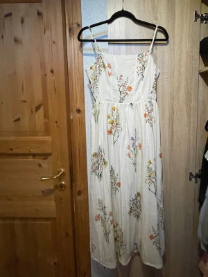 Blommig sommarklänning  - Superfin vit långklänning med smala axelband och blommigt mönster i flera färger. Liten i storleken, jag brukar ha xs men denna är s. Aldrig använd.