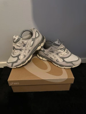 Gråa ASICS sneakers mesh och mocka - Snygga sneakers från ASICS i grått och vitt med klassisk logga på sidan. Skorna har en sportig design med mesh och mockadetaljer, samt en robust sula för extra komfort. Perfekta för dig som gillar streetwear och sportig stil.