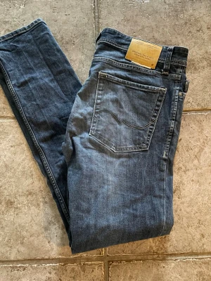 Mörkblå jeans från Jack & Jones - Snygga mörkblå jeans från Jack & Jones med klassisk femficksdesign och raka ben. Jeansen har en diskret tvätt och är tillverkade i bomull med en liten mängd stretch för extra komfort. Perfekta för en avslappnad och stilren look.