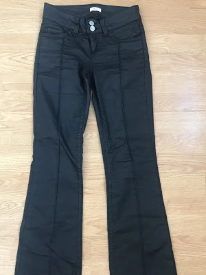 Svarta bootcut jeans med dubbla knappar - Snygga skin svarta bootcut jeans med dubbla silverknappar i midjan och markerade sömmar. Jeansen har två bakfickor med vågig brodyr och är tillverkade i ett stretchigt material för skön passform. Sitter perfekt.