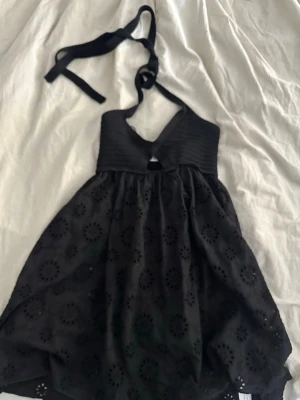 Svart halterneckklänning klänning Zara - Snygg svart kortklänning med halterneck och broderade blommönster. Klänningen har en liten öppning framtill och knyts i nacken. Perfekt för dig som vill ha en stilren och trendig look.