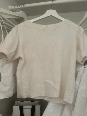Vit stickad t-shirt - Kortärmad stickad t-shirt i mjuk vit ullmix från Gina tricot. Tröjan har bred ribbad halsringning och ribbade muddar vid ärmslut och nederkant. Perfekt för lager på lager och enkel att styla till olika outfits.