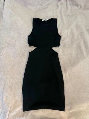 Svart cut out klänning - Snygg svart ärmlös klänning med cut out-detaljer i midjan. Klänningen är kort och har en tight passform som framhäver figuren. Har ett litet hål (se bild 3) inget man tänker mycket på men går att sy ihop! Annars fint skick! Köp direkt för 99kr😍
