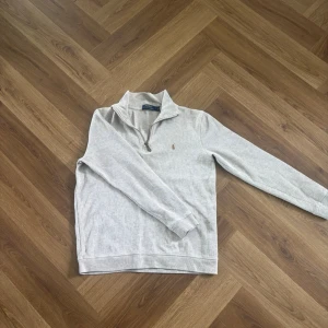 Beige Ralph Lauren halvzip - Säljer en stilren och klassisk halvzip-tröja från Polo Ralph Lauren i beige färg. Tröjan har en minimalistisk design med broderad logga på bröstet och passar perfekt både till vardag och en mer uppklädd look.