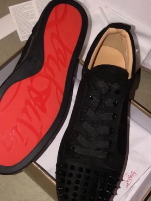 Svarta Louboutin sneakers med nitar - Säljer ett par svarta sneakers från Christian Louboutin med klassisk röd sula och svarta nitar på tån. Skorna har svarta skosnören, svart ovandel i mocka och beige insida. Perfekta för dig som vill sticka ut med en edgy och lyxig stil. (Kommer utan box) Priser går att diskutera 