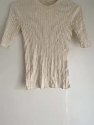 Ribbad beige t-shirt med trekvartsärm - Snygg ribbad t-shirt i beige med trekvartsärm och rund hals. Storlek S men funkar definitivt som M,inte så figurnära och ganska lös. 