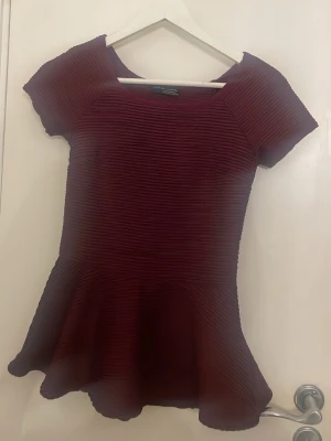 Vinröd klänning från Zara - Vinröd klänning från Zara med korta ärmar och rund halsringning. Klänningen har ett ribbat tyg med struktur och en utställd kjol som ger en snygg siluett. Perfekt för dig som gillar trendiga och feminina plagg.