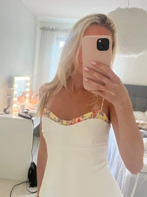 Topp från Zara - Säljer en söt vit linnetopp med smala axelband och blommigt mönster längs urringningen. Toppen har en figurnära passform och är perfekt för varma dagar. Superfin att styla med jeans eller kjol!