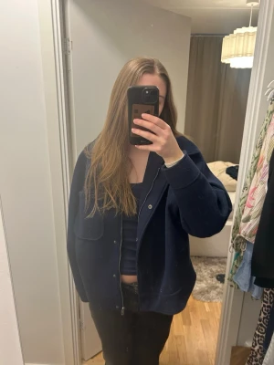 Mörkblå jacka med ficka - Säljer en mörkblå jacka med klassisk krage och en stor bröstficka. Jackan har en loose passform och stängs med knappar framtill. Perfekt att slänga över en hoodie eller t-shirt!