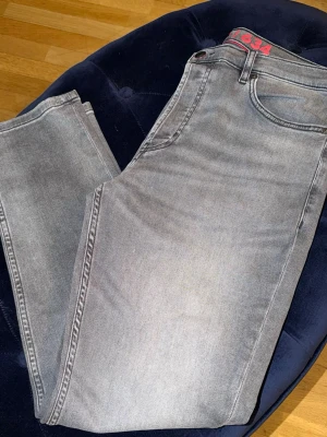 Gråa raka jeans från boss  - Snygga grå jeans från 1634 med rak passform och klassisk femficksdesign. Jeansen har en diskret tvättad look och detaljer i rött vid linningen. Perfekta för en avslappnad och trendig stil.