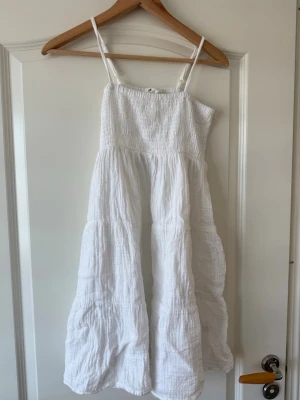 Vit sommarklänning från H&M - Luftig vit klänning från H&M med smala axelband och rynkad överdel. Klänningen har en avslappnad passform och är tillverkad i mjuk bomull, perfekt för varma dagar. Den har en lätt volang i kjolen och är enkel att styla med sandaler eller sneakers. Den passar också perfekt nu till sommaren💕💕☀️☀️
