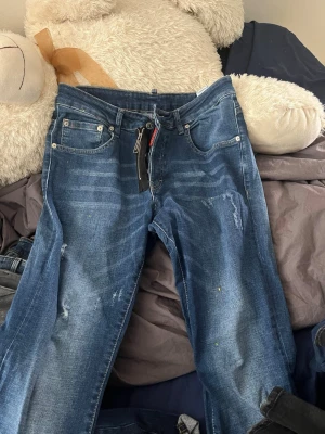 Blå jeans från Dsquared2 - Säljer ett par blå jeans från Dsquared2 med slitna detaljer och klassisk femficksmodell. Jeansen har en rak passform och cool patch med 'DAN CATEN' på baksidan. Materialet är denim i bomull och färgen är mellanblå med ljusa tvättade partier.