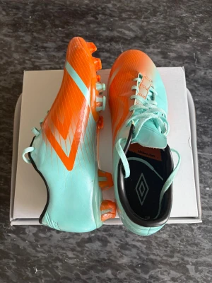 Mintgröna och orange Umbro fotbollsskor - Snygga fotbollsskor från Umbro i mintgrönt och orange med vita detaljer. Skorna har klassisk snörning, låg profil och dobbar för spel på gräs. Elites fotbollskor med väldigt bra kvalité. Sitter sköna och lätt att spela med. Nypris är mellan 1500-2000kr