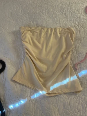 Beige tubtopp i bomull - Snygg beige tubtopp i mjukt bomullsmaterial. Enkel och stilren design utan axelband, perfekt att matcha med olika outfits. Toppen har en bandeauformad passning och är lätt att bära till både jeans och kjol.