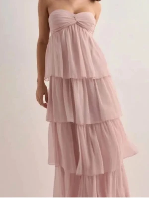 Ljusrosa långklänning med volanger - Superfin ljusrosa långklänning med flera lager volanger och knytband i midjan. Perfekt för en bal,fest eller för sommaren. Klänningen är luftig och bekväm. Klänningen är S men kan även passa som XS. Priset går att diskutera💕