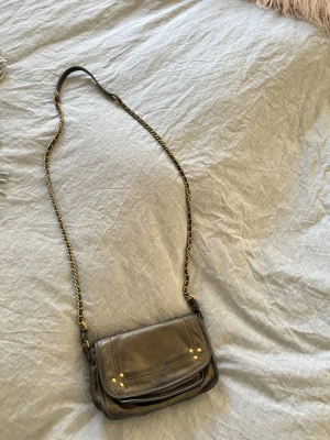 Svart/grå axelväska med guldkedja - Snygg gråsvart Jerome Dreyfuss väska i läder med guldfärgade detaljer och kedjerem. Väskan har dragkedjefack på baksidan och framsidan. Perfekt lite mindre väska men kommer inte till användning av mig.