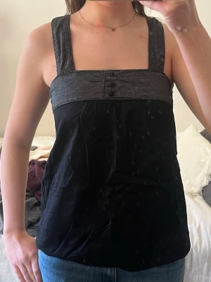 Svart linnetopp med breda axelband - Snygg svart linnetopp med breda, glittriga axelband och dekorativa knappar framtill. 