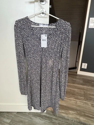 Blommig kortklänning från Mango - Supersöt kortklänning från Mango med mörkblå botten och små vita blommor. Klänningen har v-ringning, långa ärmar och en figurnära passform som ger en snygg siluett. Perfekt för dig som gillar trendiga och feminina plagg.