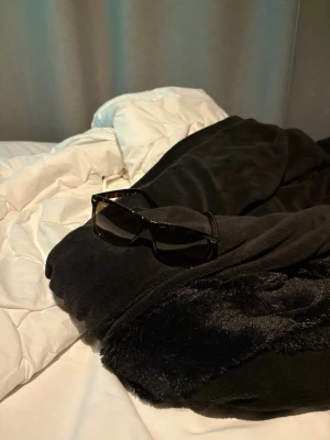 Svarta Ray-Ban solglasögon - Snygga svarta solglasögon från Ray-Ban med klassisk rektangulär form. Bågarna är i svart plast och glasen är mörka. Medföljer gör ett svart Ray-Ban fodral i skinn. Perfekta för att höja din stilnivå i solen.