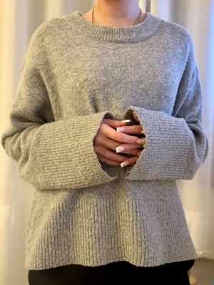 Grå stickad tröja - Mysig grå stickad tröja med vanlig passform och extra vida ärmar. Tröjan har ribbstickade muddar vid ärmslut och nederkant samt rund halsringning. Perfekt för lager på lager och chill stil.