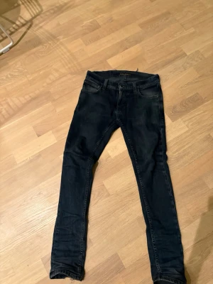 Mörkblå skinny jeans från Nudie - Säljer ett par mörkblå skinny jeans från Nudie Jeans med klassisk femficksmodell och dragkedja. Jeansen har en tight passform och subtila slitningar för en snygg look. Perfekta till sneakers eller boots. 1 litet hål vid backfickan