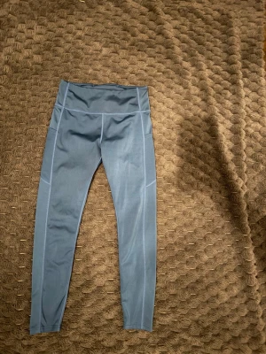 Blå sportleggings med ficka - Snygga blå sportleggings med hög midja och praktisk sidoficka. Tillverkade i stretchigt funktionsmaterial som passar perfekt för träning eller chill. Sömmen längs benen ger en sportig look och materialet känns mjukt mot huden.