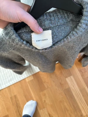 Grå stickad tröja från A Day March - Mysig grå stickad tröja från A Day March med rund halsringning och långa ärmar. Tröjan har en klassisk, enkel design med ribbade muddar vid ärmslut och nederkant. Perfekt för lager-på-lager och chill dagar. Storlek L men passar mer åt M