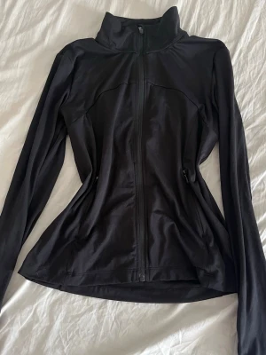 Svart träningsjacka med dragkedja - Snygg svart träningsjacka med hel dragkedja framtill och hög krage. Jackan har långa ärmar och figurnära passform, perfekt för löpning eller gym. Tillverkad i ett stretchigt funktionsmaterial som andas.