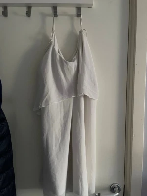 Vit somrig klänning med öppen rygg - Säljer en vit somrig med öppen rygg  tunna, korsade axelband och v-ringning. Materialet ser ut att vara ett lätt tyg, perfekt för sommaren. Enkel och stilren design som passar till många tillfällen.