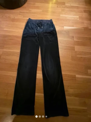 Svarta mjukisbyxor i velour - Säljer ett par svarta juicy mjukisbyxor i mjuk velour med raka ben och bred resår i midjan. Byxorna har dragsko och två stora fickor fram. Perfekta för chill dagar eller när du vill vara extra bekväm. Byxorna har lite slittage vid knäna, men inget som märks mycket. Använda ett fåtal gånger
