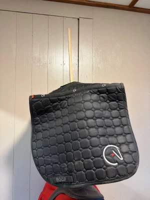 Svart schabrak från EGO7 - Säljer ett svart schabrak från EGO7 med broderad logga i vitt och rött. vadderat för extra komfort till hästen. Passar perfekt till tävlingoch träning. Strl full svart. Kan säljas billigare vid snabb affär☺️