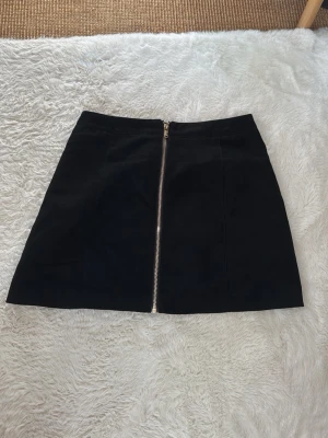 Svart kortkjol med dragkedja - Snygg svart kortkjol i mockaimitation med en silverfärgad dragkedja framtill. Från h&m i storlek 38