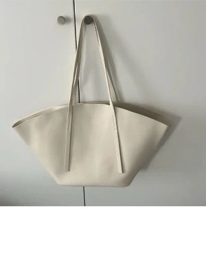 Beige shoppingväska i konstläder - Stilren shoppingväska i beige konstläder med långsmala axelband och minimalistisk design. Väskan har en rymlig insida och en liten innerficka. Perfekt för dig som gillar enkel och modern stil.