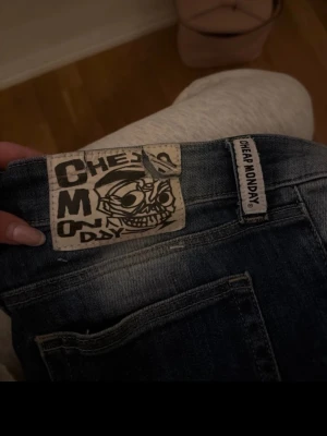 Blå jeans från Cheap Monday - Säljer ett par klassiska blå jeans från Cheap Monday med deras ikoniska döskalle-logga på bakfickan. Jeansen har en smal passform och är tillverkade i denim med snygga slitningar och tvättade detaljer. Perfekta för en avslappnad och trendig look.