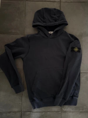 Stone island hoodie - Snygg mörkgrå hoodie från Stone Island i storlek 12-14 år och passar någon mellan 155-166 cm. Den är stilren och passar perfekt till vardags. Den är självklart äkta och går äkthets verifiera genom CLG coden i tröjan. (Pris går självklart att diskuteras vid snabb affär!)