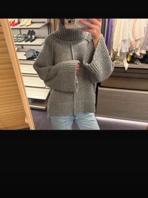 Grå oversized stickad polotröja - Säljer en grå oversized stickad polotröja med breda ärmar och ribbade muddar. Tröjan har en hög polokrage och är gjord i ett mjukt, tjockt material som passar perfekt för kyliga dagar. Enkel och stilren design som är lätt att matcha.