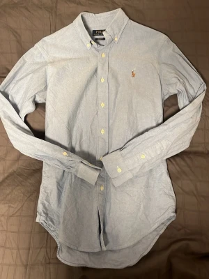 Ralph Lauren Skjorta - Tja säljer nu en Ljusblå Ralph Lauren Skjorta i ett fint skick utan några defekter. Hör av dig vid frågor eller funderingar.