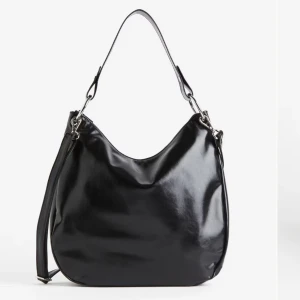 Svart axelväska i skinn - Säljer en snygg och stilren svart axelväska i skinn. Väskan har en enkel design med en bred axelrem och en extra lång rem för att bära den över kroppen. Perfekt för både vardag och fest!💕