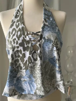 Leopardmönstrad halterneck topp Glitzy London - Snygg halterneck topp från Glitzy London med leopardmönster i blått, vitt och grönt. Toppen har snörning framtill och är tillverkad i ett glansigt, mjukt material som känns lyxigt. Perfekt för dig som vill sticka ut med coola detaljer och unik mix av mönster.