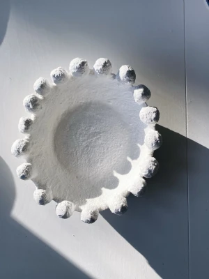 Vit dekorativ skål med bollar - Unik vit skål i lera med rund form och dekorativa bollar längs kanten. Skålen har en ”stenliknande” yta och konstnärlig design som gör den till ett snyggt inslag i hemmet, perfekt som dekoration eller förvaring av småsaker.