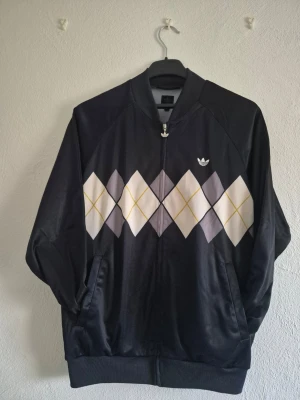 Vintage adidas zip up  - Ovanlig (Ivan Lendl edition) mörkblå ziptröja från Adidas med argylemönster i vitt, grått och gult över bröstet och ryggen. Tröjan har ribbade muddar och två fickor framtill. Materialet är glansigt och ger en sportig känsla. Perfekt för dig som gillar retrostil och streetwear.
