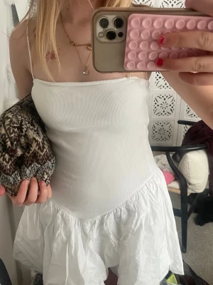 Vit kort klänning med tunna band - Supersöt vit kort klänning med tunna axelband och volangkant nedtill. Klänningen har en figurnära passform upptill, perfekt med en kofta eller tröja när det blir kallare på kvällarna!💕storleken är S men passar som en XS. Perfekt att ha på sig när det är skolavslutning, student, midsommar eller bara ha på sig på en vanlig dag💝