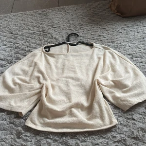 Beige topp med vida ärmar från 157 - Säljer en beige topp från 157 med vida, trekvartsärmar och rak halsringning. Materialet känns mjukt och har en lätt struktur, perfekt för en avslappnad men ändå stilren look. Passar dig som gillar minimalistisk och enkel design.