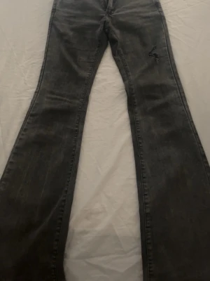 Grå bootcut jeans med slitning - Säljer ett par grå bootcut jeans med en cool sliten detalj på låret. Jeansen har en klassisk femficksmodell och är tillverkade i denim med lätt stretch. Perfekta för dig som gillar en avslappnad och trendig look.